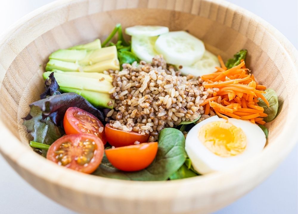 Salade composée dans un bol avec riz brun, œuf, avocat, concombre et légumes, adaptée pour un régime pauvre en glucides.