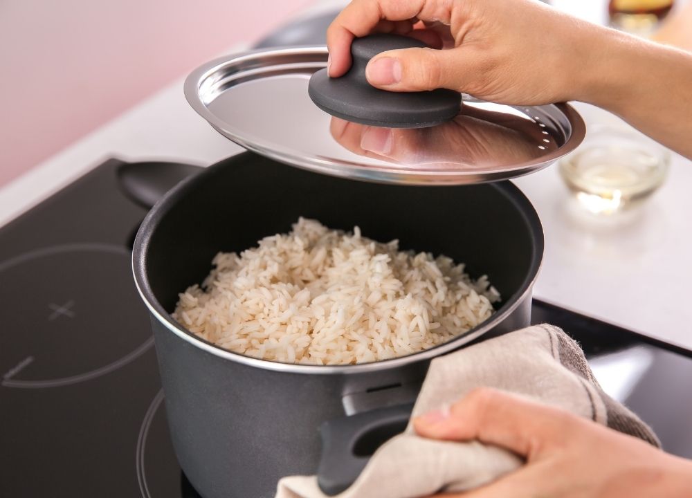 Une main soulève le couvercle d'une casserole de riz cuit.