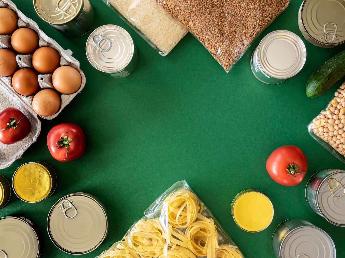 Produits alimentaires essentiels sur fond vert : œufs, conserves, tomates, pâtes, riz, pois chiches, et concombre