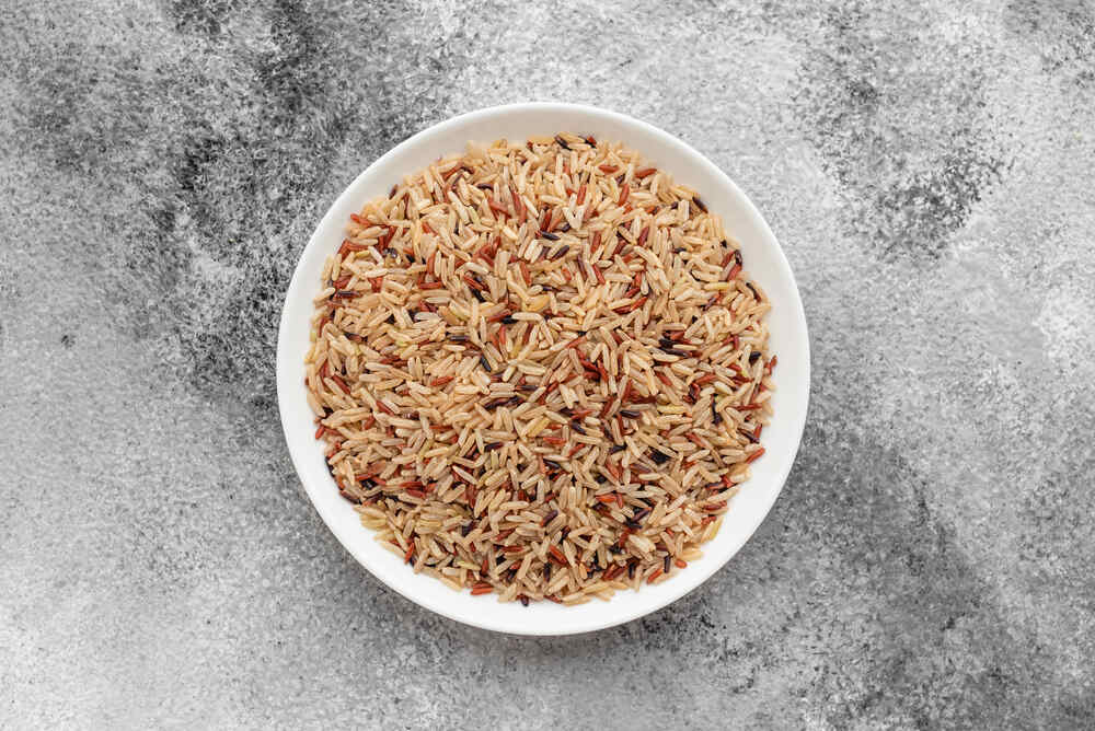 Mélange de riz (riz brun, riz sauvage, etc.) dans un bol blanc sur un fond gris texturé.