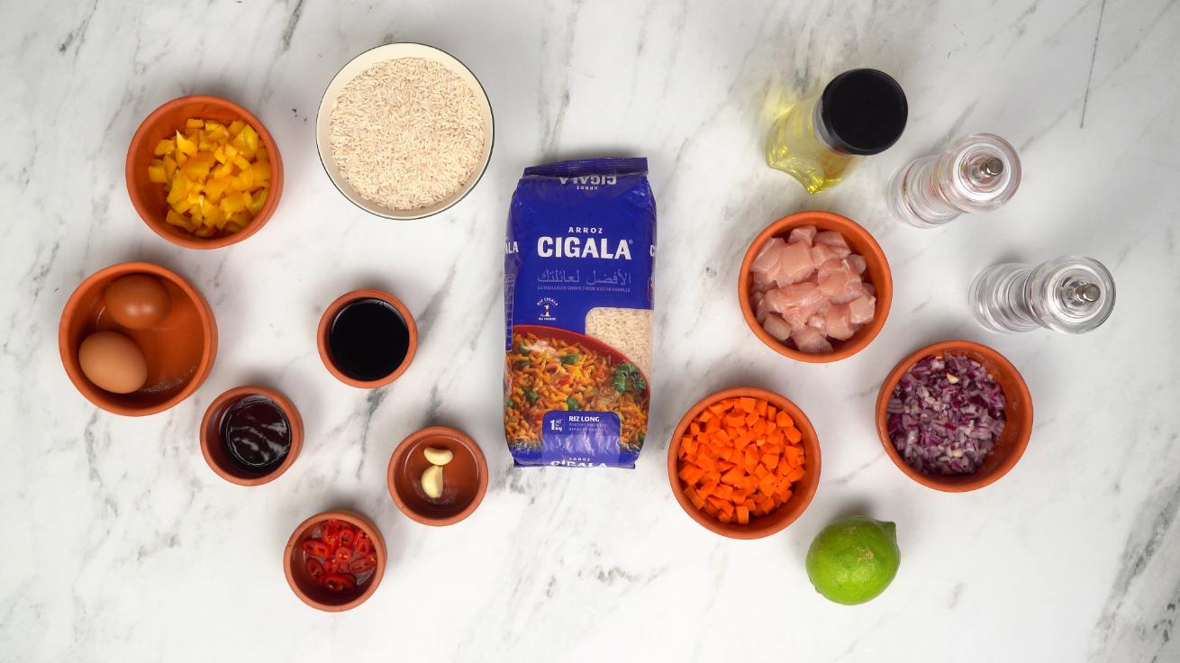 ngrédients disposés pour la préparation du Nasi goreng : riz Cigala, poulet, légumes coupés, œufs, sauces et citron vert.