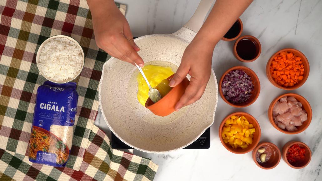 Versement de l'œuf battu dans une poêle chaude pour le faire brouiller, une étape essentielle de la recette de Nasi goreng.