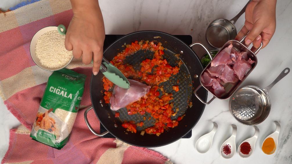  Des morceaux de lapin sont ajoutés aux légumes déjà sautés dans la poêle, prochaine étape de la cuisson de la paella.