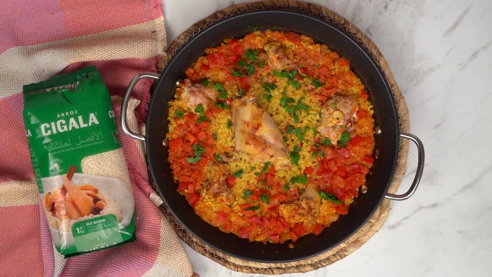 Une paella au lapin, riche en couleurs avec son riz doré, ses légumes rouges et ses morceaux de lapin, est prête à être dégustée dans une grande poêle.