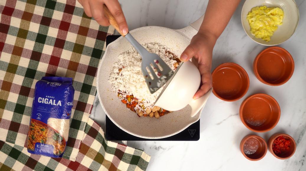 Incorporation du riz cuit dans la poêle avec le mélange de poulet et légumes, pour créer le riz frit Nasi goreng.