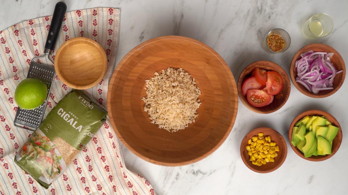 Riz complet Cigala cuit dans un grand saladier en bois, prêt à être mélangé avec les tomates, l'avocat et le maïs.