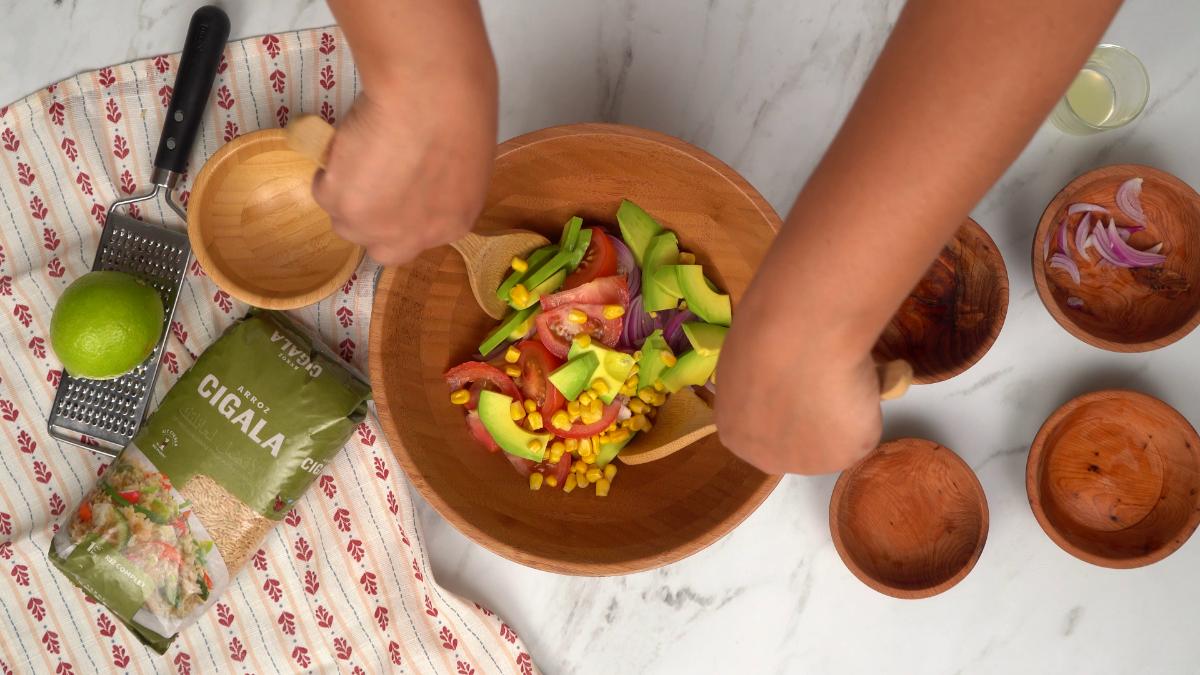 Mélange des ingrédients de la salade d'avocat et de tomate avec le riz dans un grand saladier en bois à l'aide de couverts à salade.