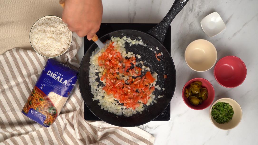 Ajout des tomates en dés aux oignons dans la poêle, une étape clé de la recette facile du riz à la mexicaine.