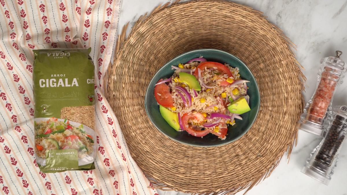  Plat final de la salade d'avocat, tomate et riz complet Cigala, servi dans un bol vert sur un set de table en osier.