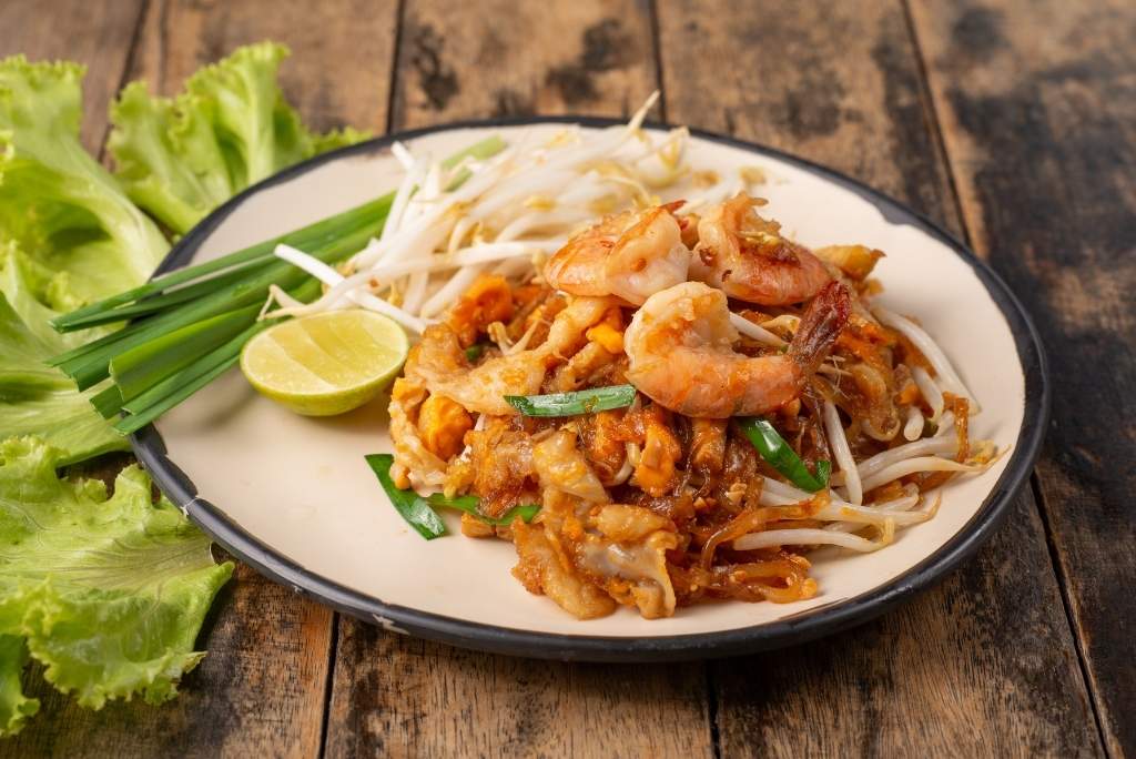 طبق باد تاي بالروبيان مُزيّن ببراعم الفاصوليا والثوم المعمّر وقطعة من الليمون الأخضر.