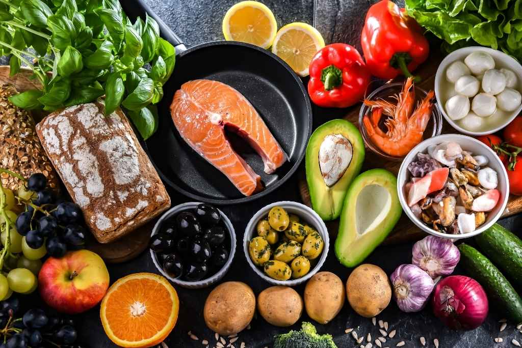 المشروبات الموصى بها: الماء، الشاي والمنقوعات منظر علوي لتشكيلة متنوعة من الأطعمة الصحية مثل السمك والفواكه والخضروات والخبز، موضوعة على خلفية داكنة.