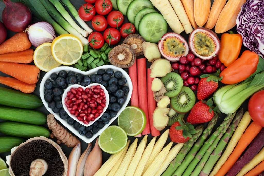 Un assortiment coloré et dense de fruits et légumes frais, avec un bol en forme de cœur rempli de baies.