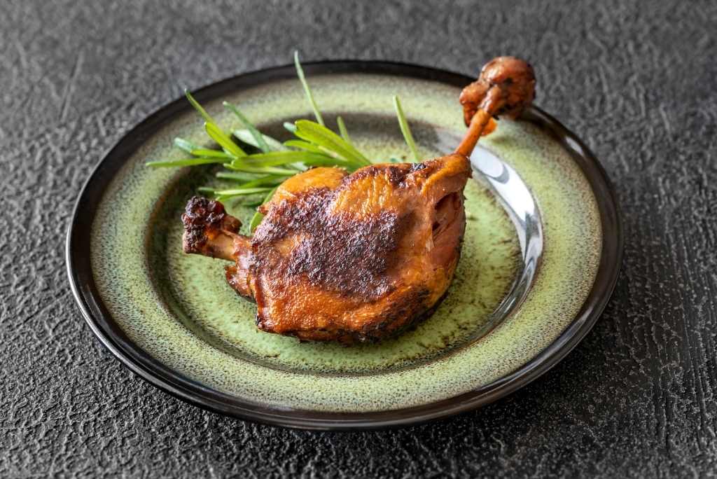 فخذ بط مُحضّر بتقنية الكونفي ومحمّر، مزين بإكليل الجبل ومقدّم على طبق خزفي.