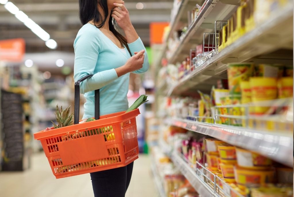 Une femme tenant un panier de courses orange dans un supermarché, en train de regarder des produits dans les rayons.