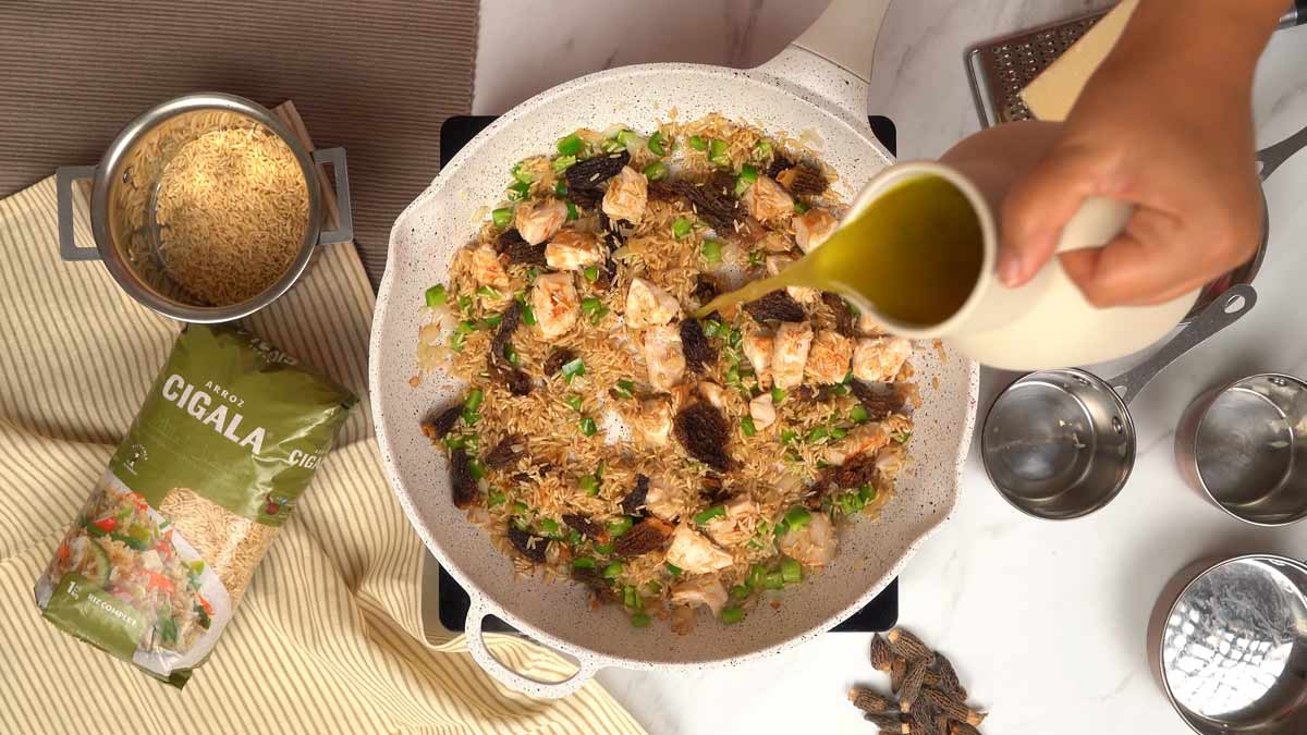 يُسكب مرق الخضار الساخن فوق خليط الأرز الكامل Arroz Cigala مع الخضار والدجاج للطهي
