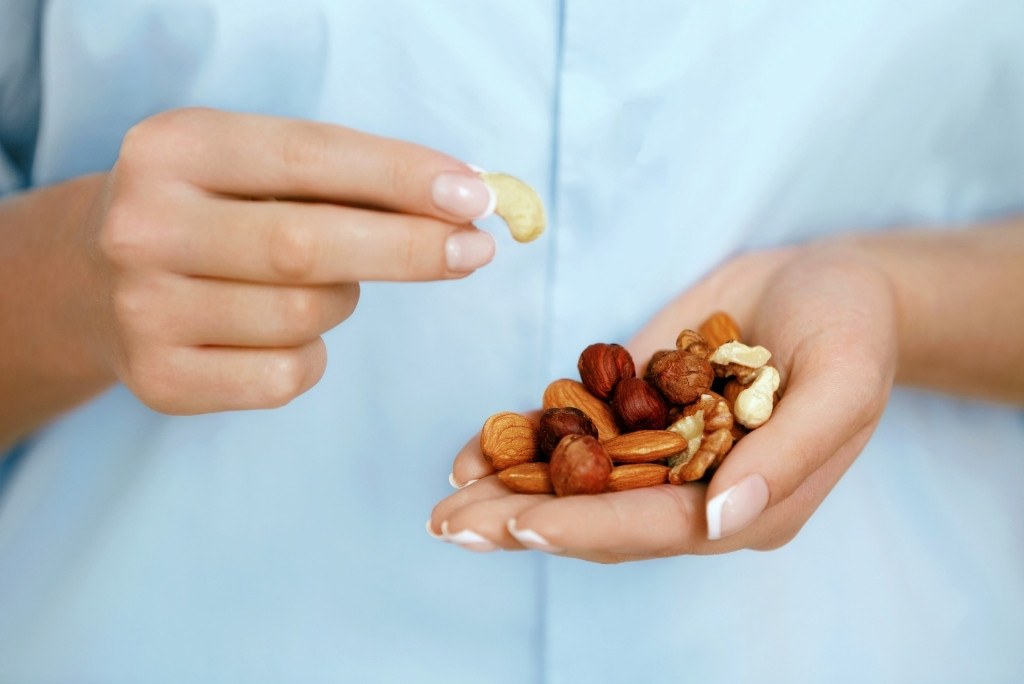Gros plan sur une main tenant une poignée de noix et d'amandes, et l'autre main tenant une seule noix de cajou.