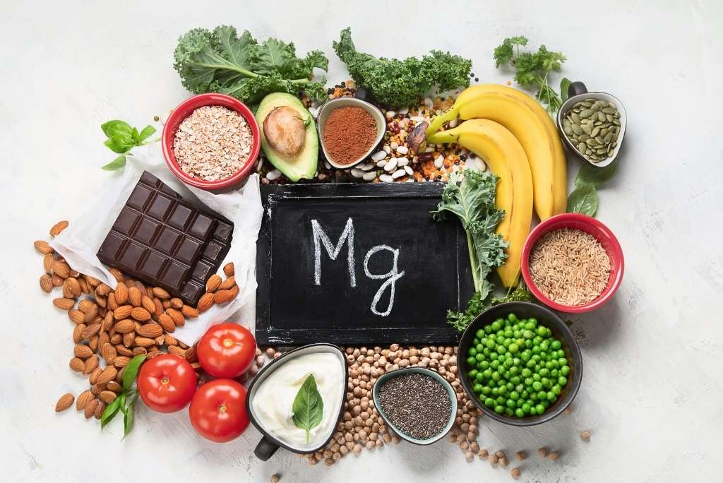 Autres facteurs influençant le sommeil منظر علوي لأطعمة غنية بالمغنيسيوم (شوكولاتة داكنة، لوز، موز، خضروات) تحيط بلافتة مكتوب عليها « Mg ».