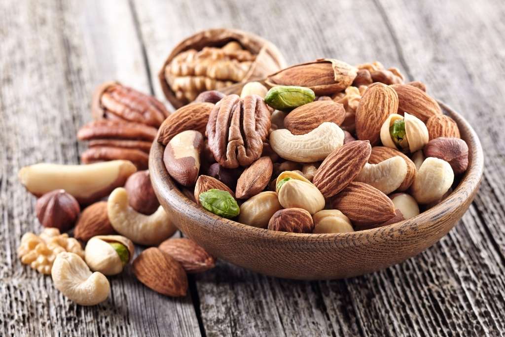 المكسرات والبذور: مصدر غني بالمغنيسيوم لقطة مقرّبة لوعاء خشبي مليء بمزيج من المكسرات (جوز البيكان، اللوز، الكاجو) على طاولة ريفية.