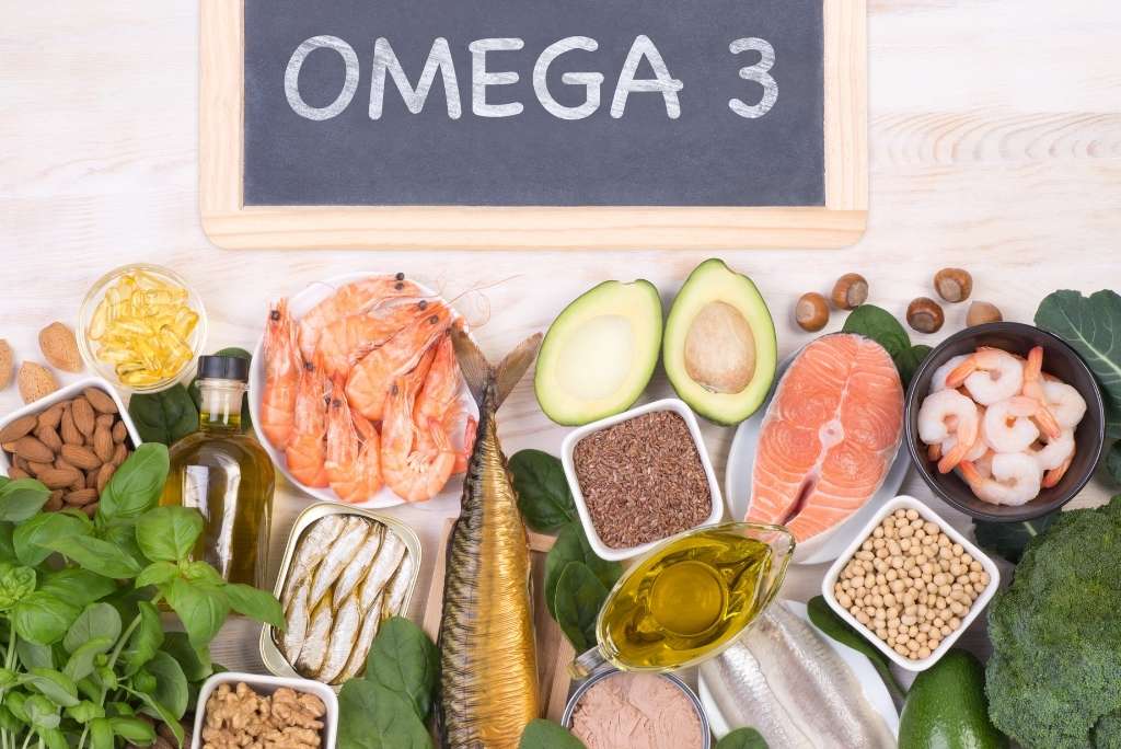 Vue d'en haut d'un assortiment d'aliments riches en oméga-3 (poissons gras, noix et avocat) disposés sous une pancarte « OMEGA 3 ».