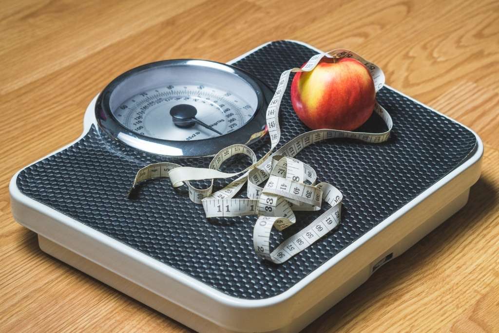 فقدان وزن صحي ومستدام ميزان وزن تعلوه تفاحة وشريط قياس، في إشارة إلى النظام الغذائي وفقدان الوزن.