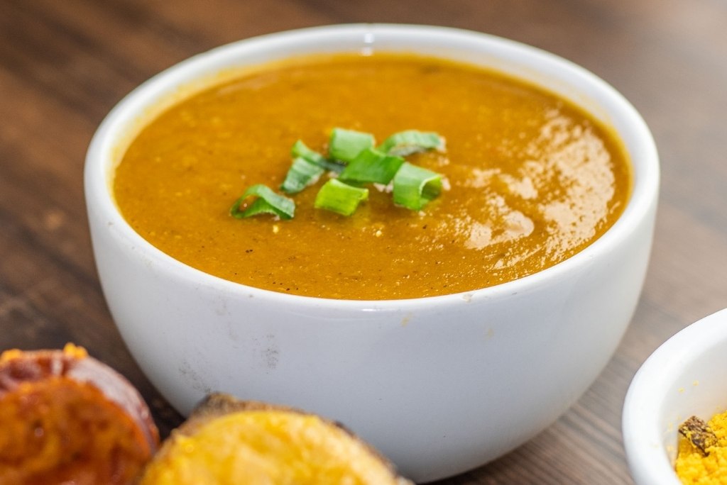 لقطة مقرّبة لوعاء من حساء أو هريس برتقالي اللون مزين ببصل أخضر مفروم.