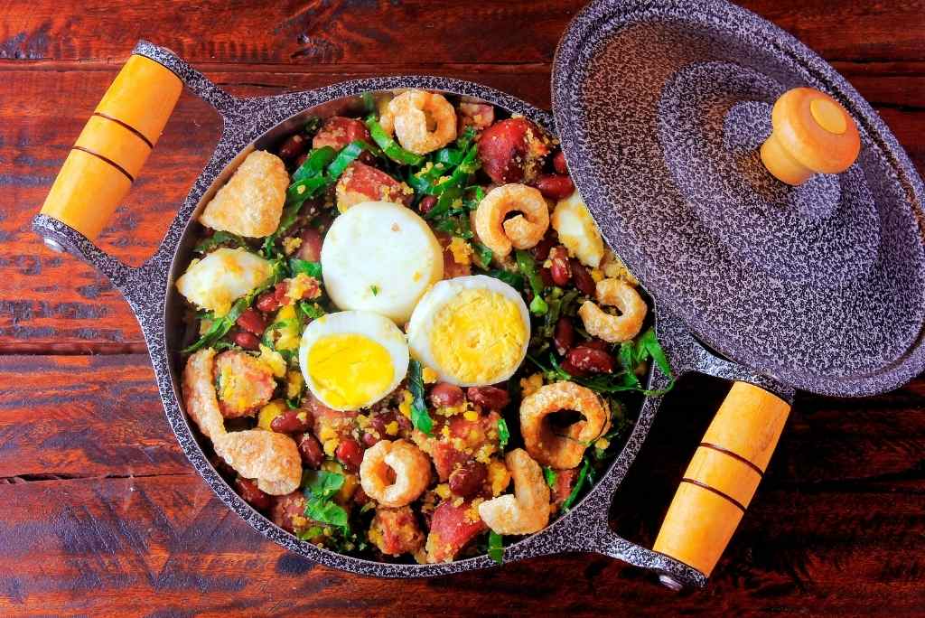 طبق فيجاو تروبيرو، طبق برازيلي نموذجي يعتمد على الفاصوليا والنقانق والكرنب والبيض، على طاولة خشبية ريفية.