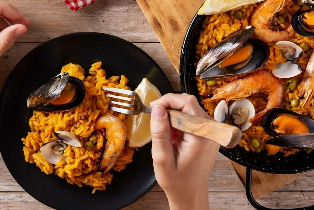 يدٌ تقدّم حصة من باييلا المأكولات البحرية في طبق أسود باستخدام شوكة.