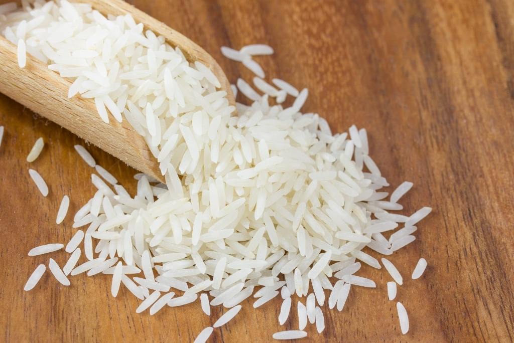 الفوائد الصحية ملعقة خشبية تحتوي على أرز أبيض متناثر فوق سطح خشبي.