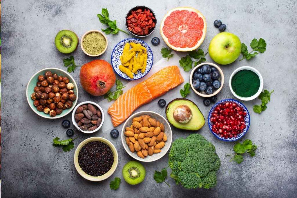 سوبرأغذية طاقية لا غنى عنها منظر علوي لتشكيلة من الأطعمة الغنية بالعناصر الغذائية (سلمون، فواكه، مكسّرات وخضروات) على خلفية رمادية.