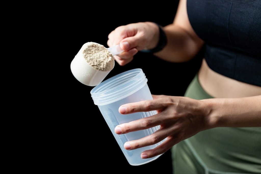 صورة مقربة لشخص يرتدي ملابس رياضية ويصب مسحوق البروتين في شيكر.
