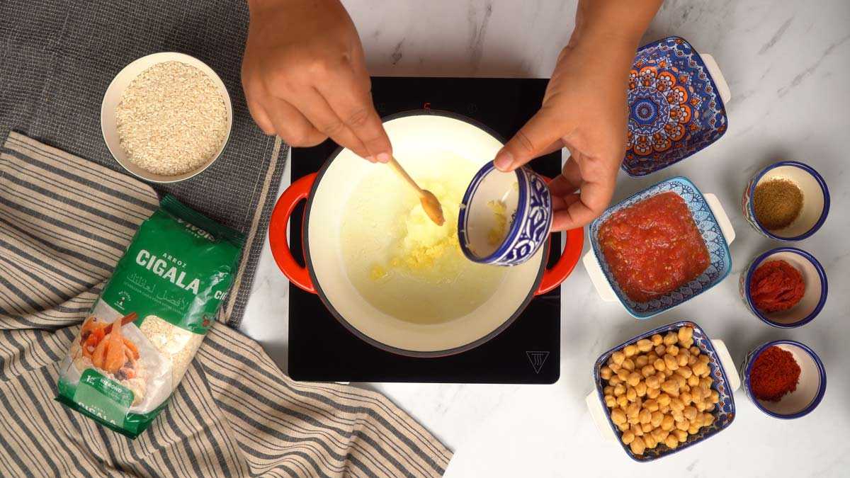 Préparer la base du plat Une personne ajoute des oignons hachés à de l'huile dans une casserole.