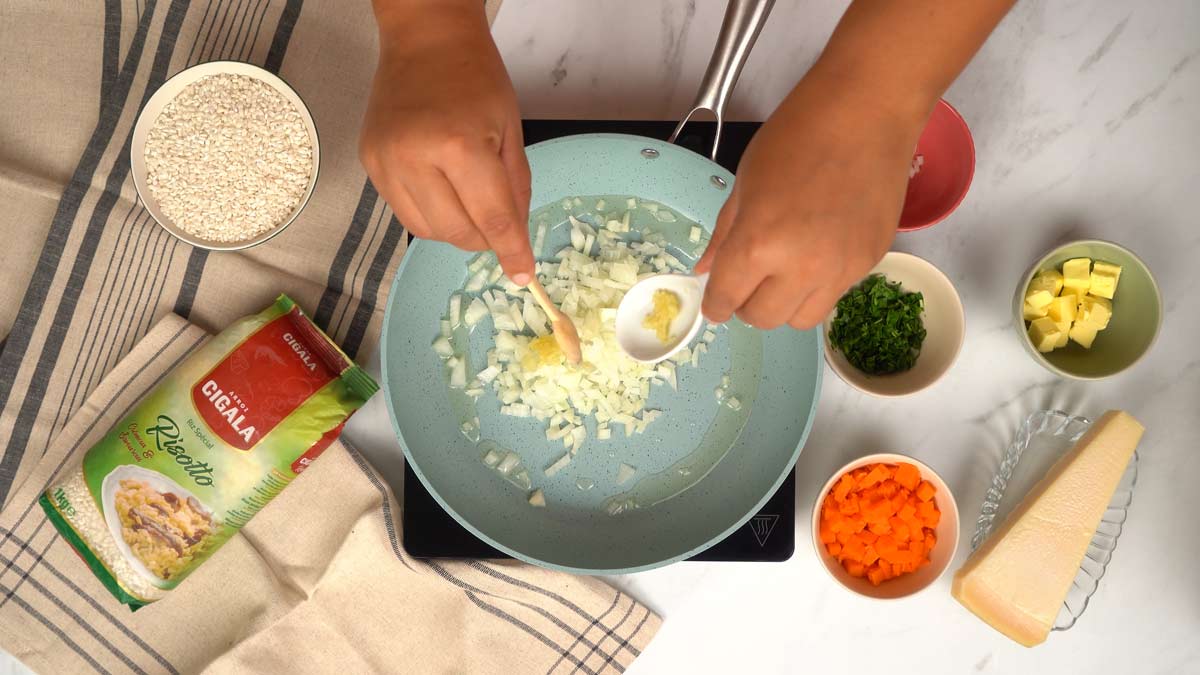 Cuire les oignons Une personne ajoute de l'ail haché aux oignons sautés dans une poêle.