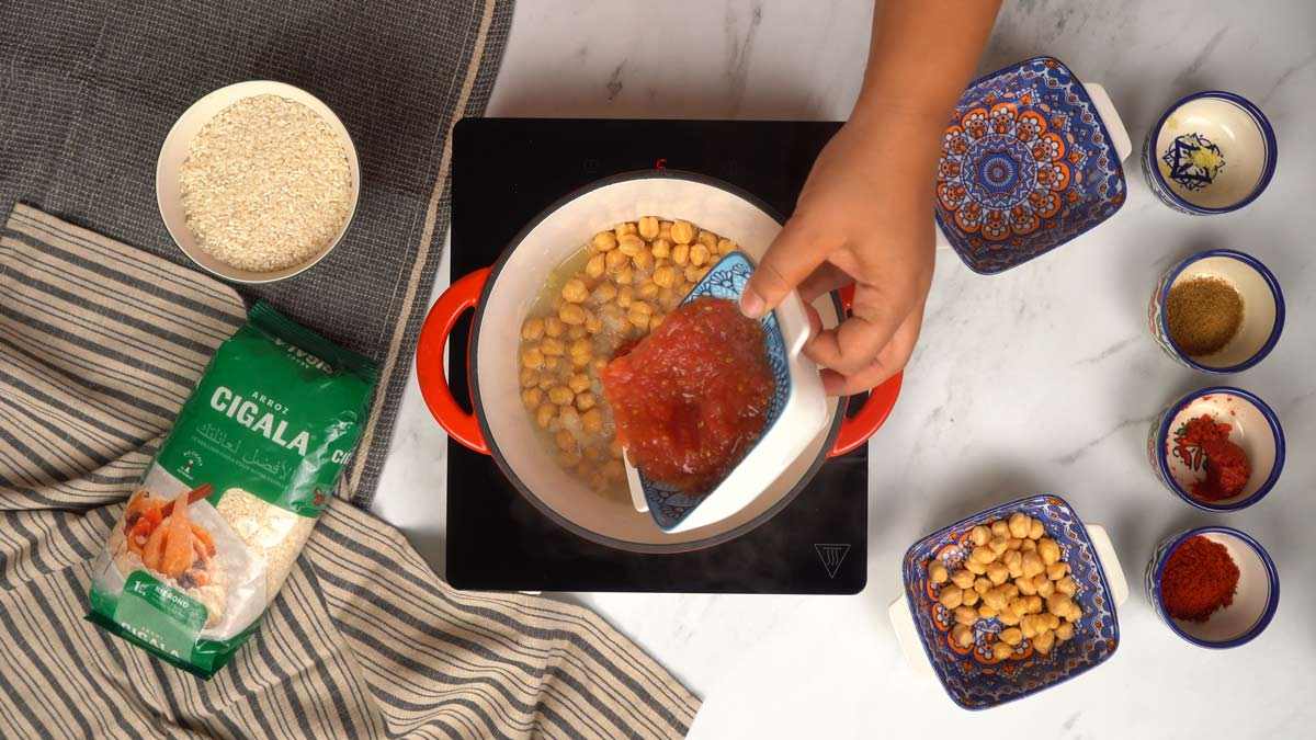 Ajouter les pois chiches et les tomates Une personne verse une louche de tomates concassées et des pois chiches dans la casserole.