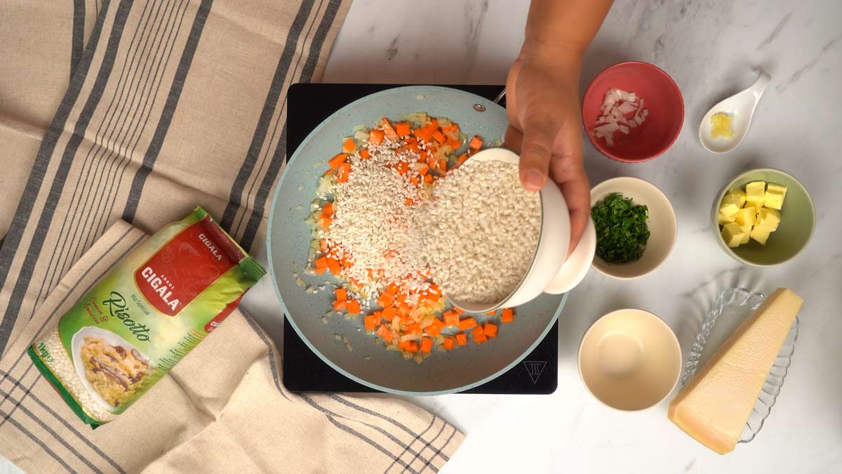 Cuire le riz à risotto Une personne verse du riz à risotto dans la poêle avec les légumes pour le nacrer.