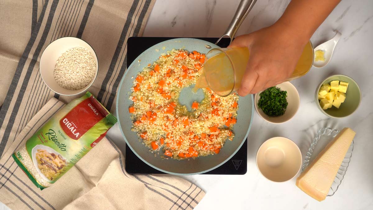Ajouter le bouillon progressivement Une personne verse du bouillon dans la poêle pour cuire le risotto.