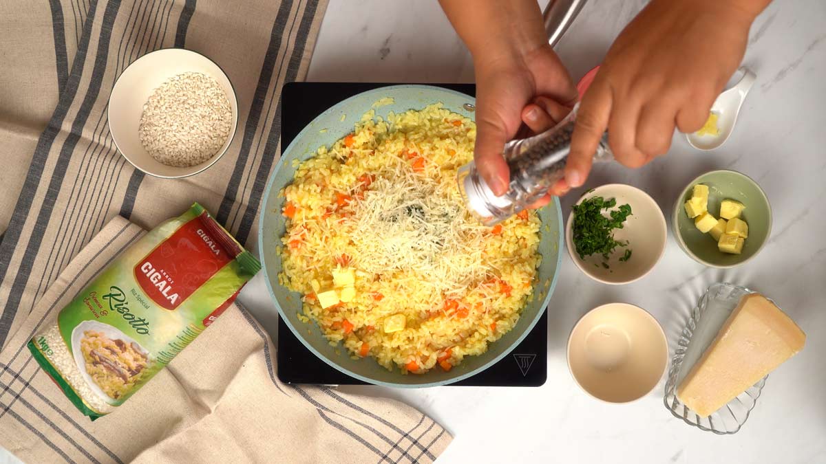 Finaliser le risotto Une personne ajoute du poivre moulu sur le risotto presque terminé, avec du fromage et du beurre.