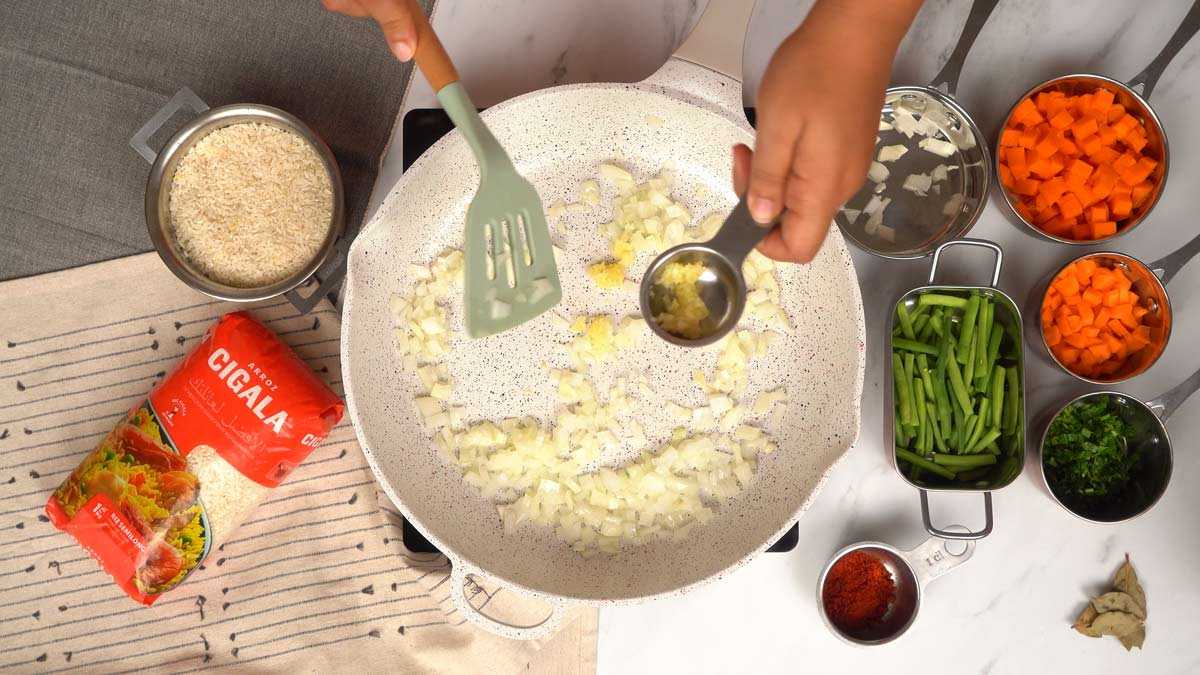 تحضير القاعدة العطرية شخص يضيف الثوم المفروم إلى البصل المقلي في المقلاة.