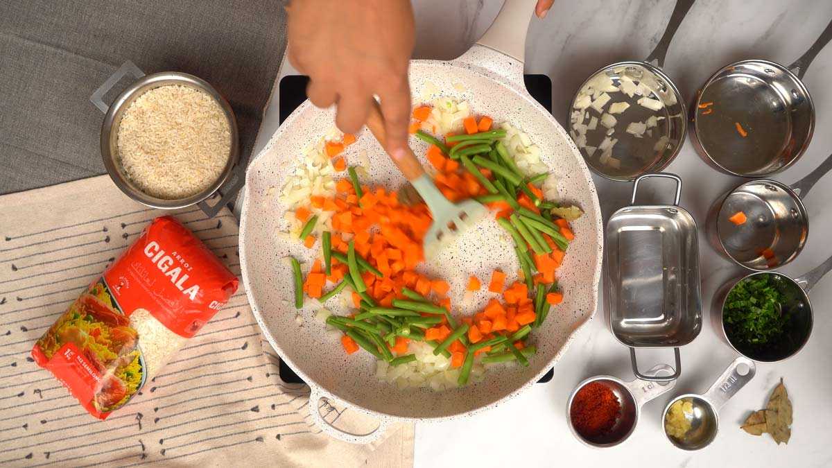 إضافة الخضروات شخص يخلط مكعبات القرع والفاصوليا الخضراء مع البصل في المقلاة.