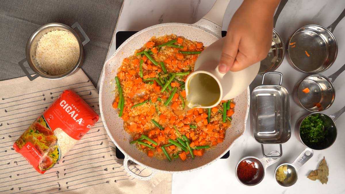 طهي الأرز شخص يصب المرق فوق الأرز والخضروات أثناء الطهي.