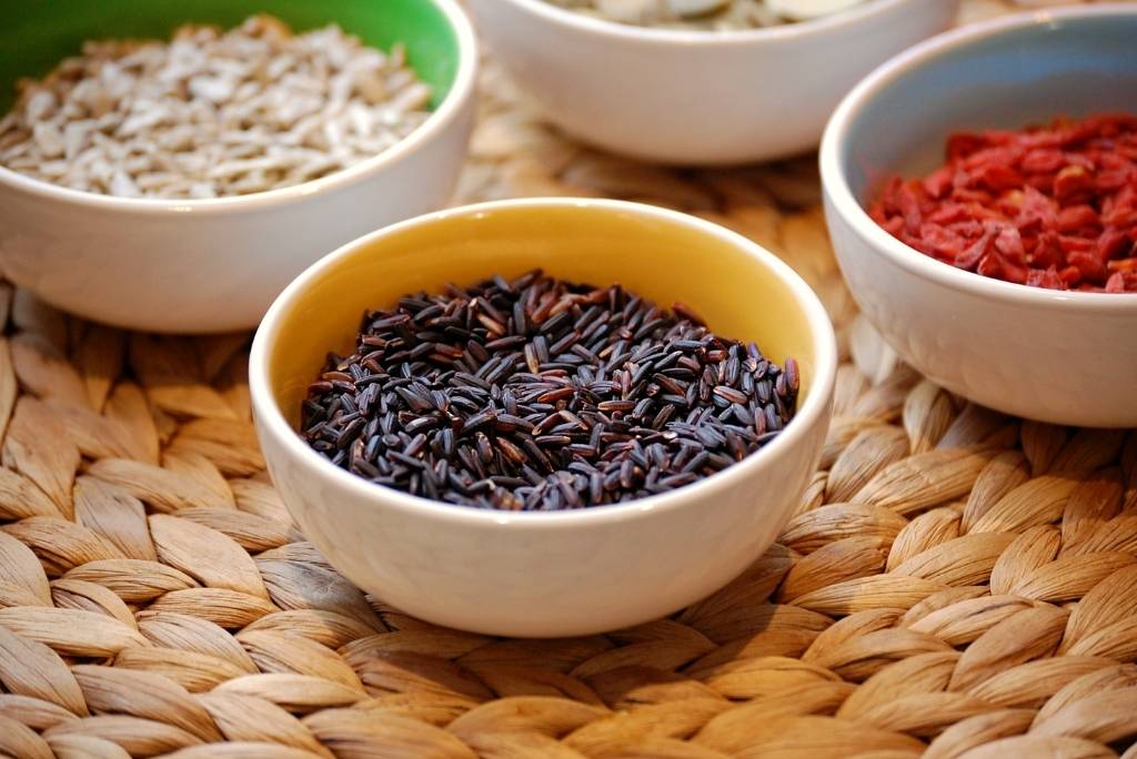 ثروة غذائية لا تُضاهى لقطة مقرّبة لوعاء من الأرز الأسود النيّئ محاط ببذور دوّار الشمس وتوت مجفف، موضوع على مفرش منسوج.