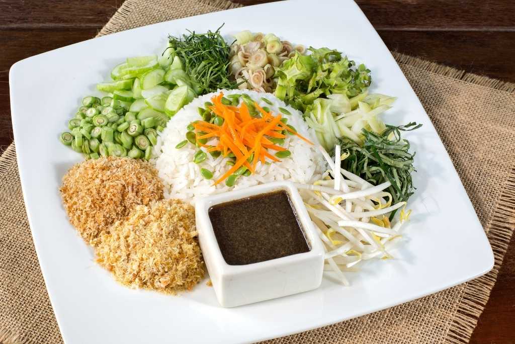 طبق خاو يام (سلطة أرز من جنوب تايلاند) مُزيّن بالأرز والأعشاب والخضار الطازجة ولحم مُفتّت وصلصة بنية، مقدّم في طبق أبيض.