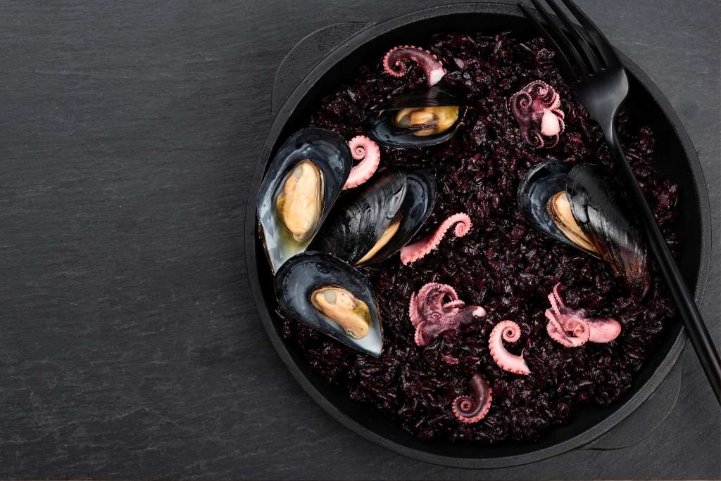 وصفة متوسطية: أرز أسود بالمأكولات البحرية طبق من الأرز الأسود مع المأكولات البحرية (بلح البحر والأخطبوط) مقدّم في طبق داكن.