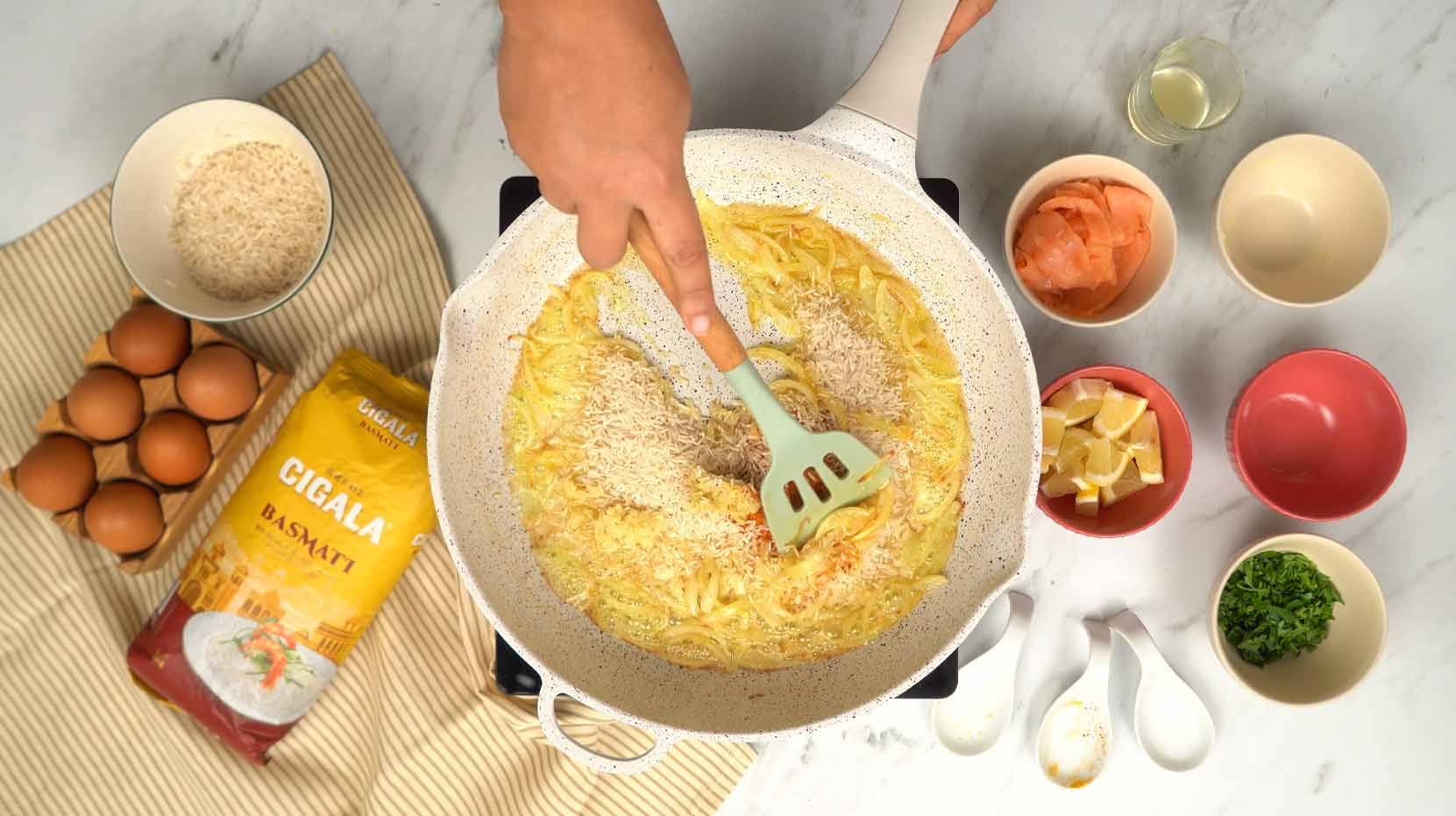 يُضاف أرز البسمتي والتوابل إلى البصل مع التحريك حتى تتغلف الحبات بالدهون والنكهات.