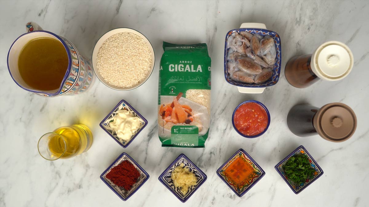 On prépare tous les ingrédients, incluant le riz rond, les petits calamars, la sauce tomate, le bouillon et l'aïoli pour la garniture.