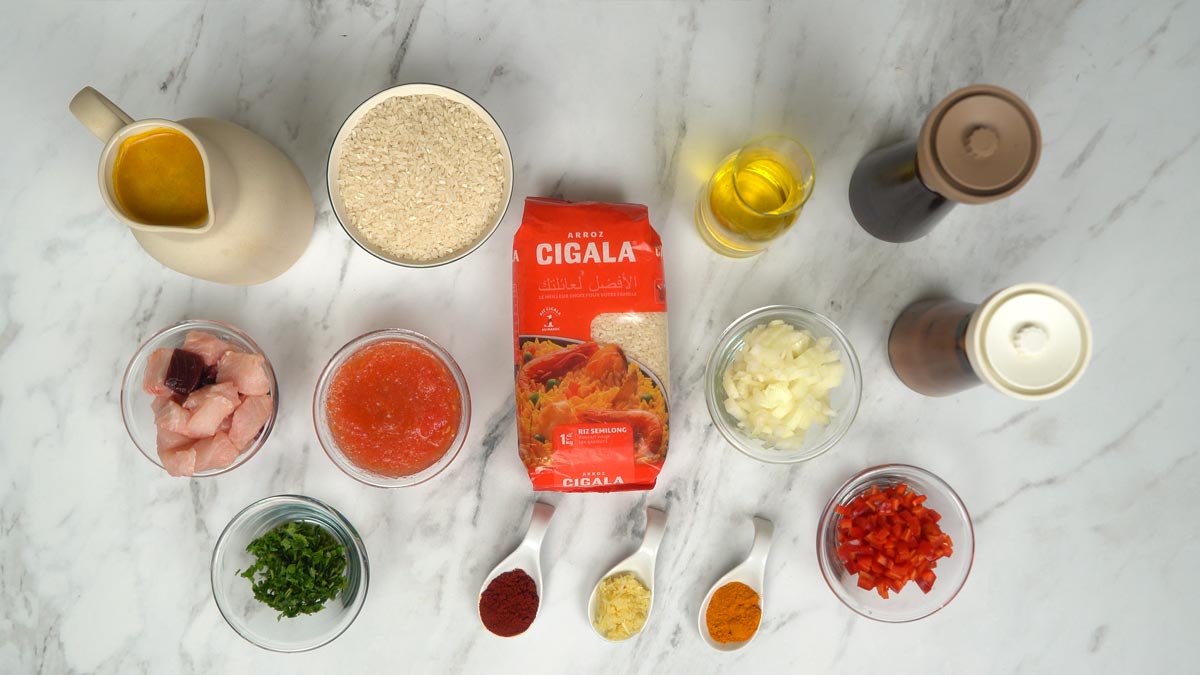 Préparation des ingrédients On prépare les ingrédients principaux, incluant des morceaux de poisson frais, du riz, de la sauce tomate, du bouillon, ainsi que divers oignons, poivrons et épices.