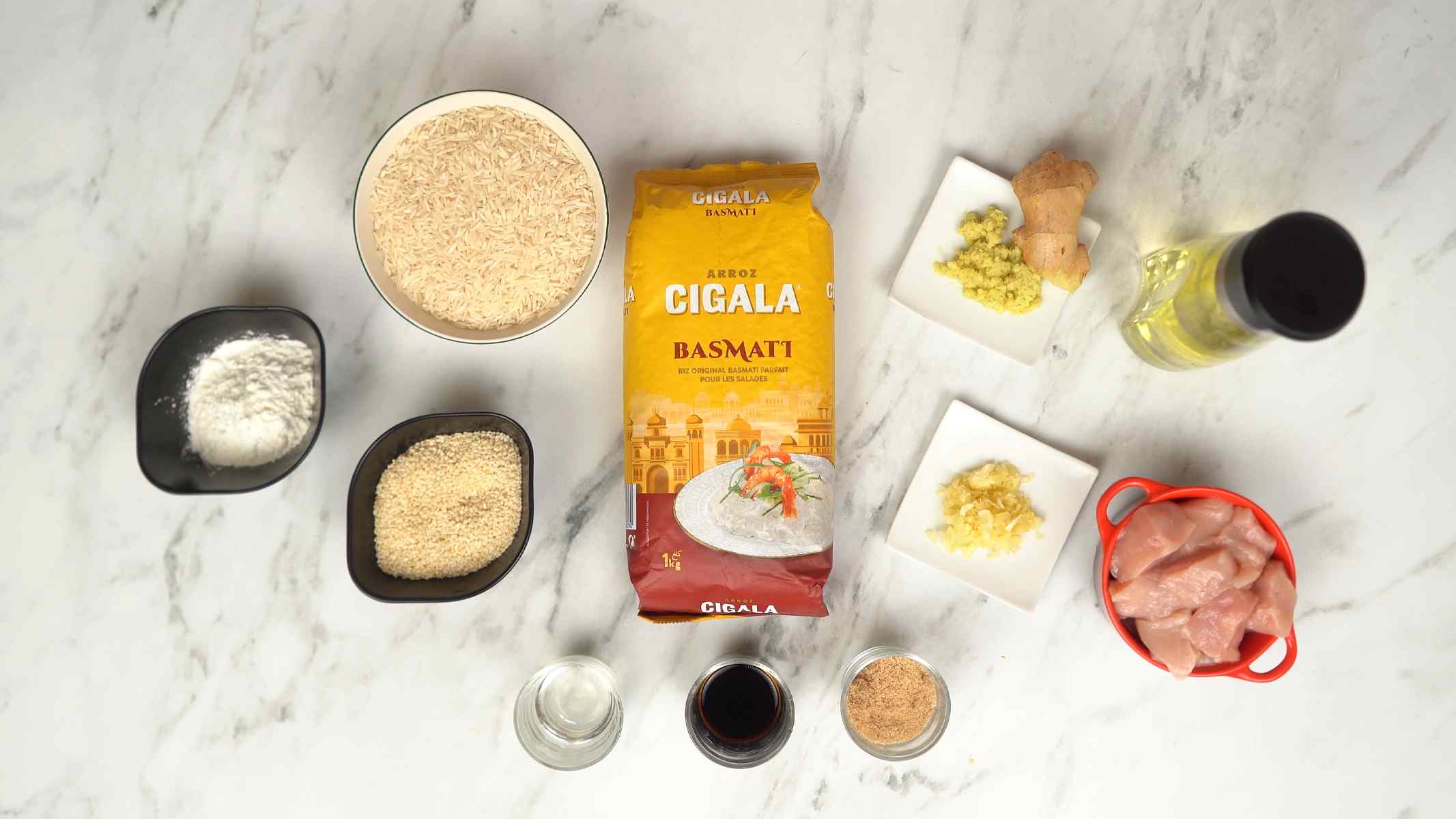 يتم تحضير المكونات، بما في ذلك الدجاج، أرز البسمتي، الزنجبيل، الثوم، صلصة الصويا وبذور السمسم.