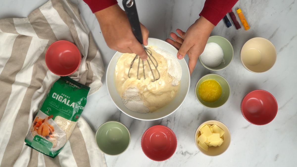 نخلط دقيق الأرز مع الحليب وباقي المكوّنات السائلة جيداً باستخدام مضرب حتى نحصل على خليط ناعم.