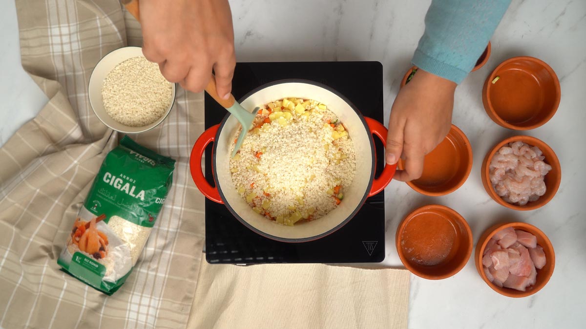 Cuisson du riz et des légumes On ajoute ensuite le riz rond aux légumes dans la marmite pour qu'il commence à s'imprégner des saveurs.
