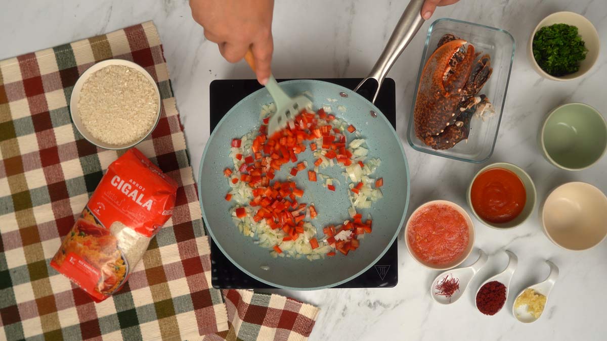 تحضير القاعدة العطرية في مقلاة، يُقلّى الفلفل الأحمر المقطّع والبصل في قليل من الزيت لتكوين قاعدة شهية.