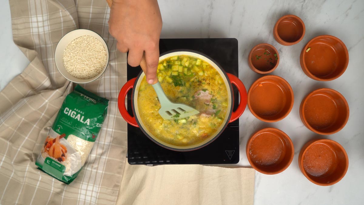 Ajout du poisson et des crevettes On verse le bouillon sur le mélange de riz, de légumes et de viande, puis on ajoute les courgettes et les herbes fraîches pour laisser mijoter le tout.